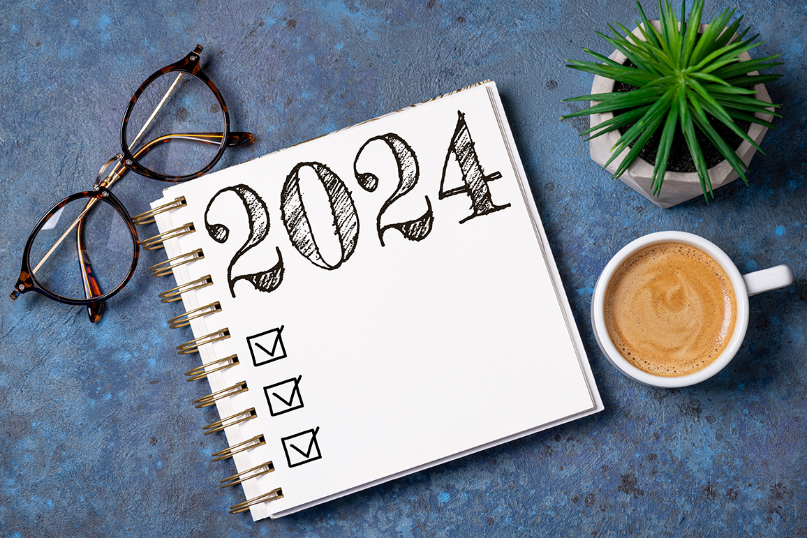 2024 goals list with notebook, coffee cup, plant on wooden table.